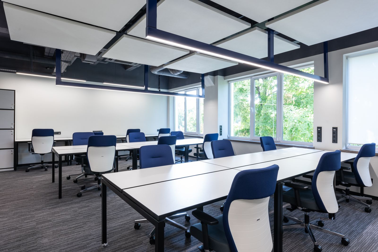 An empty open-plan office with white desks, blue chairs and a window
