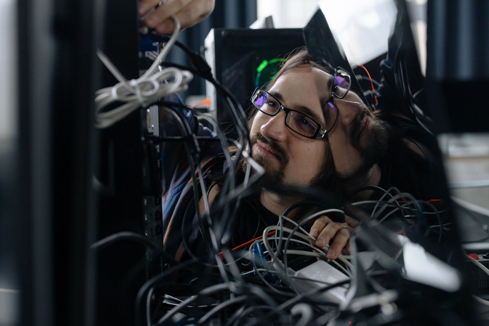 A man peers through a tangle of cables beside a computer tower